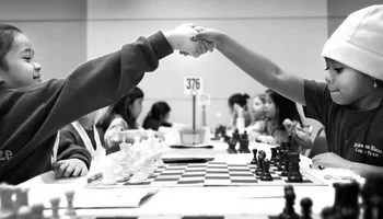 Two girls shaking hands at the start of a chess game 