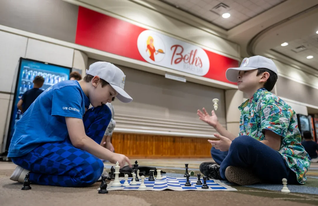 Two kids playing chess, one tossing a piece in the air