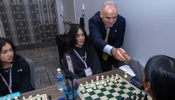 Garry Kasparov, making the first move for WIM Iris Mou on board one, shakes hands with Sanushya Subramaniam